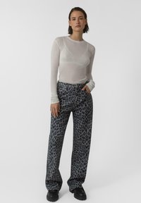 Top lungo bianco trasparente a maniche lunghe e pantaloni larghi grigi con stampa leopardata. I pantaloni hanno una vestibilità ampia e una leggera texture. Stivali neri completano l'outfit.