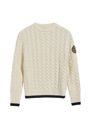 Kremowy sweter z grubym splotem warkoczowym, z prążkowanymi mankietami i obrębem, czarną lamówką oraz naszywką na lewym rękawie.