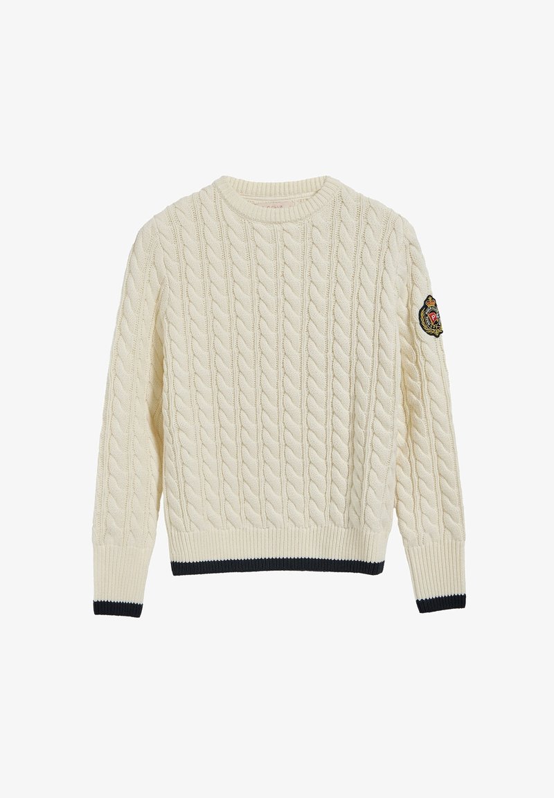 Pull crème en maille torsadée avec poignets et ourlet côtelés, bordure noire, et écusson brodé sur la manche gauche.