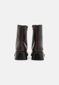 Brown leather ankle boots with a smooth finish, zip closure at the back, and sturdy, textured black heel. Sleek and minimal design.