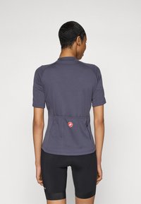 Maillot de cyclisme à manches courtes en tissu bleu foncé, doté d'une poche zippée et d'un logo rouge près de la taille. Le design comprend des manches raglan.