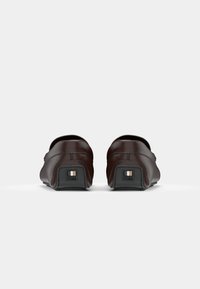 Mocassins en cuir marron avec un design arrondi, présentant une texture lisse, des coutures contrastées et un petit logo en accent au talon.