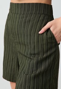 Shorts plissés verts en tissu texturé. Présentent une taille haute et une poche latérale, mettant en avant un design structuré.