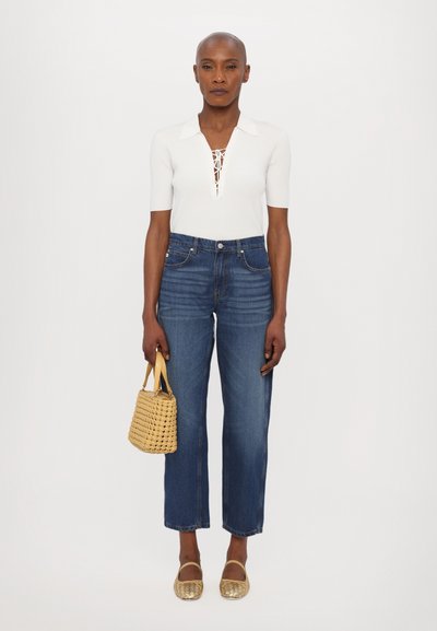 Polo blanco de punto acanalado con detalle de cordones, jeans rectos azul, bailarinas metálicas doradas y un pequeño bolso tejido dorado.