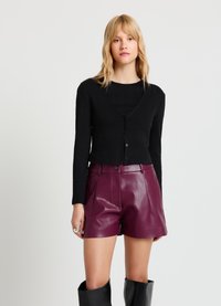 Cardigan noir côtelé avec col en V et fermeture à boutons, associé à un short taille haute en similicuir bordeaux. Texture lisse et coupe ajustée.