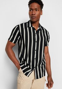 Chemise à manches courtes avec des rayures verticales noir et crème, dotée d'un col pointe et d'une texture de tissu lisse.
