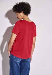 Chemise rouge à manches courtes avec un col rond, texture douce et fentes sur les côtés, assortie à un jean en denim bleu ample.