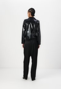Veste noire, brillante, surdimensionnée au motif serpent, associée à un pantalon noir ample. Comprend des épaulettes et un design court.