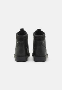Botas de cuero negra hasta el tobillo con punta redondeada, cuello acolchado y lengüetas en la parte posterior. Presentan una superficie texturizada y suela de goma plana.