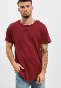 Bordeaux kortærmet t-shirt lavet af blød bomuld, med en rund halsudskæring og en afslappet pasform. Bæres med lyseblå denimjeans.