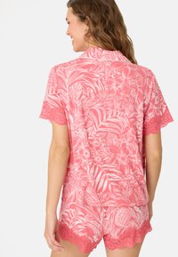 Roze bloemenpyjama set met korte mouwen en shorts. Stof heeft een gladde textuur met kantafwerking aan de mouwen en de zoom.