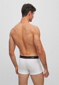 Boxer briefs de algodón blancos con una cinturilla negra que presenta el logo de BOSS, mostrados desde la vista trasera de una persona con cabello corto.
