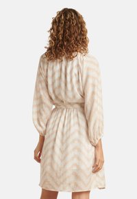 Musterkleid mit einem Zickzackdesign in hellbeige und cremefarbenen Tönen, mit Puffärmeln und einem Gürtel in der Taille.