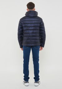 Giacca piumino navy con colletto alto e design trapuntato, abbinata a jeans in denim blu e sneakers nere con accenti bianchi.