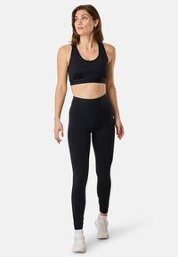 Musta urheilBra ja korkeavyötäröiset legginssit joustavasta materiaalista, joissa on saumanomaton muotoilu ja sileä pinta, yhdistettynä valkoisiin tennareihin.