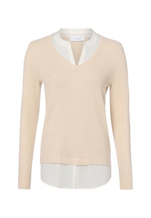 Crèmekleurige gebreide trui, laagjes over een witte blouse met V-halsdetail en lange mouwen.
