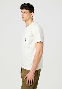 Hvid bomulds T-shirt med korte ærmer, der har en brystlomme og et lille logopatch. Bæres sammen med olivengrønne cargo bukser.