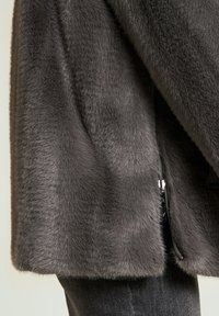 Grijze jas van nepbont met een zachte textuur, voorzien van een zijritssluiting en een rechte afwerking aan de zoom, gecombineerd met donkere spijkerbroek.