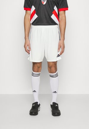 Abbigliamento da calcio maschile composto da una maglia nera con accenti rossi e bianchi, pantaloni corti bianchi e scarpe da calcio nere con calzettoni a strisce bianche.