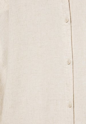 Țesătură bej din in cu textură vizibilă și trei nasturi mici bej aliniați vertical pe o pată de cămașă.