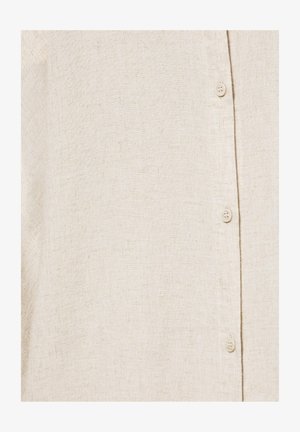 Țesătură bej din in cu textură vizibilă și trei nasturi mici bej aliniați vertical pe o pată de cămașă.