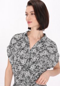 Cămașă scurtă cu mânecă, cu un model floral alb-negru, având guler, tăietură lejere și detaliu de talie strânsă. Textură de material neted.
