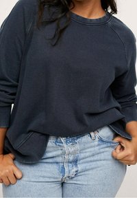 Felpa a maniche lunghe di un blu scuro con maniche raglan, texture morbida e vestibilità comoda, abbinata a jeans chiari a vita alta.