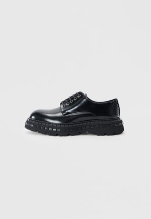 Black leather dress shoe with a rounded toe, six eyelets, and a thick black textured sole featuring a treaded pattern.