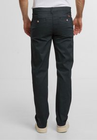 Dunkelgraue Hose aus strukturiertem Stoff, gerader Schnitt, zwei Gesäßtaschen und dezente Metallakzente. Sichtbare Nähte an verschiedenen Stellen.