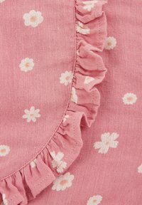 Tejido rosa con un patrón floral que presenta pequeñas flores blancas y un borde con volantes. Material texturizado similar al lino. Diseño circular.