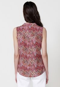 Top senza maniche con motivo zigzag multicolore che presenta tonalità di rosa, marrone e crema. Tessuto morbido con orlo arrotondato e dettagli sul retro.