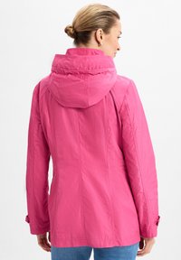 Rosa wasserdichte Jacke mit hohem Kragen und verstellbarem Kapuzen, seitlichen Taschen und Knopfakzenten an den Ärmel, glatte Oberfläche.