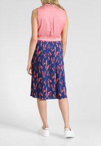 Ärmlös rosa topp med en plisserad marinblå kjol med ett blommönster i röd och rosa, kombinerad med vita sneakers.