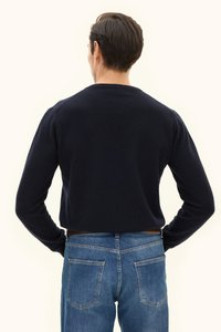 Marineblauwe gebreide trui met lange mouwen, ronde halslijn en een gestructureerde afwerking, gecombineerd met blauwe spijkerbroek met achterzakken.