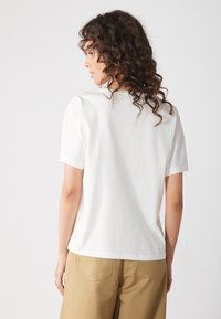 Maglietta bianca a maniche corte realizzata in morbido cotone con scollatura rotonda, caratterizzata da una vestibilità comoda e da una texture liscia.