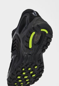 Semelle noire de chaussure de course Nike avec des accents jaunes antidérapants et un marquage visible sur les crampons et la semelle intermédiaire.