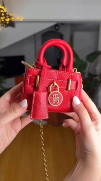 Κόκκινη δερμάτινη τσάντα με χρυσά μεταλλικά στοιχεία, μικρού μεγέθους, με λεπτομέρεια κλειδαριάς, διπλές λαβές και λουρί αλυσίδα. Ορατή υφή επιφάνειας.