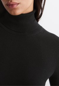 Zwarte geribbelde turtleneck trui met een aansluitend ontwerp, textuurstof en verticale lijnen die de halslijn en schouders accentueren.