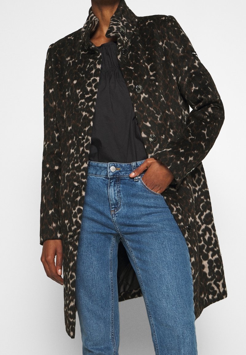 Djurprintad kappa i mörkbruna och svarta toner, med hög krage, texturerat tyg och svarta knappar, kombinerad med ljusblå jeans.