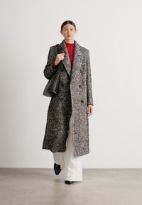 Kabát s herringbone vzorem v mnoha barvách, dvouvrstvý design s velkými klopy. Kombinován s červeným topem a černou taškou.