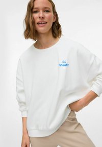 Sudadera blanca de corte holgado, con el texto azul "Italia TOSCANA" en la parte delantera. Puños y cuello acanalados. Textura suave.