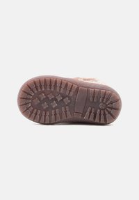 Semelle de chaussure en caoutchouc brun avec un motif texturé, dotée de crans multidirectionnels pour une adhérence et d'un talon arrondi.