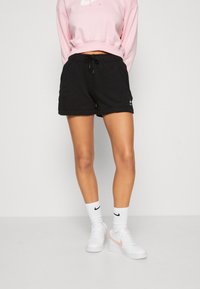 Černé sportovní šortky s tkaničkou v pase, spárované s růžovým svetrem. Bílá ponožky a bílé tenisky s růžovými akcenty dokončují vzhled.