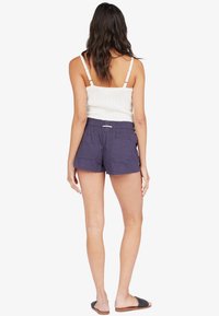 Shorts en mélange de coton bleu marine avec une taille élastique et deux poches arrière, associés à un débardeur blanc à côtes et des sandales plates.