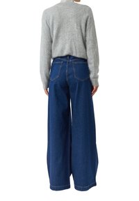 Jasnoszary, puszysty sweter w połączeniu z luźnymi, wysokim stanem, ciemnoniebieskimi dżinsami. Charakterystyczne detale to duże tylne kieszenie i szerokie nogawki.