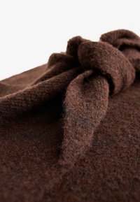 Posnetek blizu rjave teksturirane volnene tkanine z velikim, mehkim vozelnim detajlom na oblačilu ali dodatku.