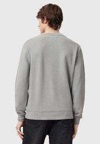 Sudadera gris con una textura suave, escote redondo y puños acanalados. La vista trasera no muestra ninguna marca ni patrones visibles. Se lleva con jeans oscuros.