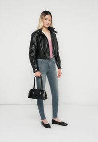 Sort cropped læderjakke, lys pink tanktop, blå skinny jeans, sorte flade sko og en lille sort håndtaske. Glatte teksturer og tætsiddende design.