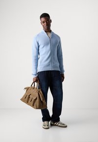 Light blue zip-up sweater, dark denim pants, beige leather bag with three front pockets, and brown sneakers with green stripes.
