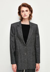 Blazer grigio a quadri con design strutturato, dotato di due tasche anteriori, bottoni rotondi e dettagli screziati su tutto il tessuto.